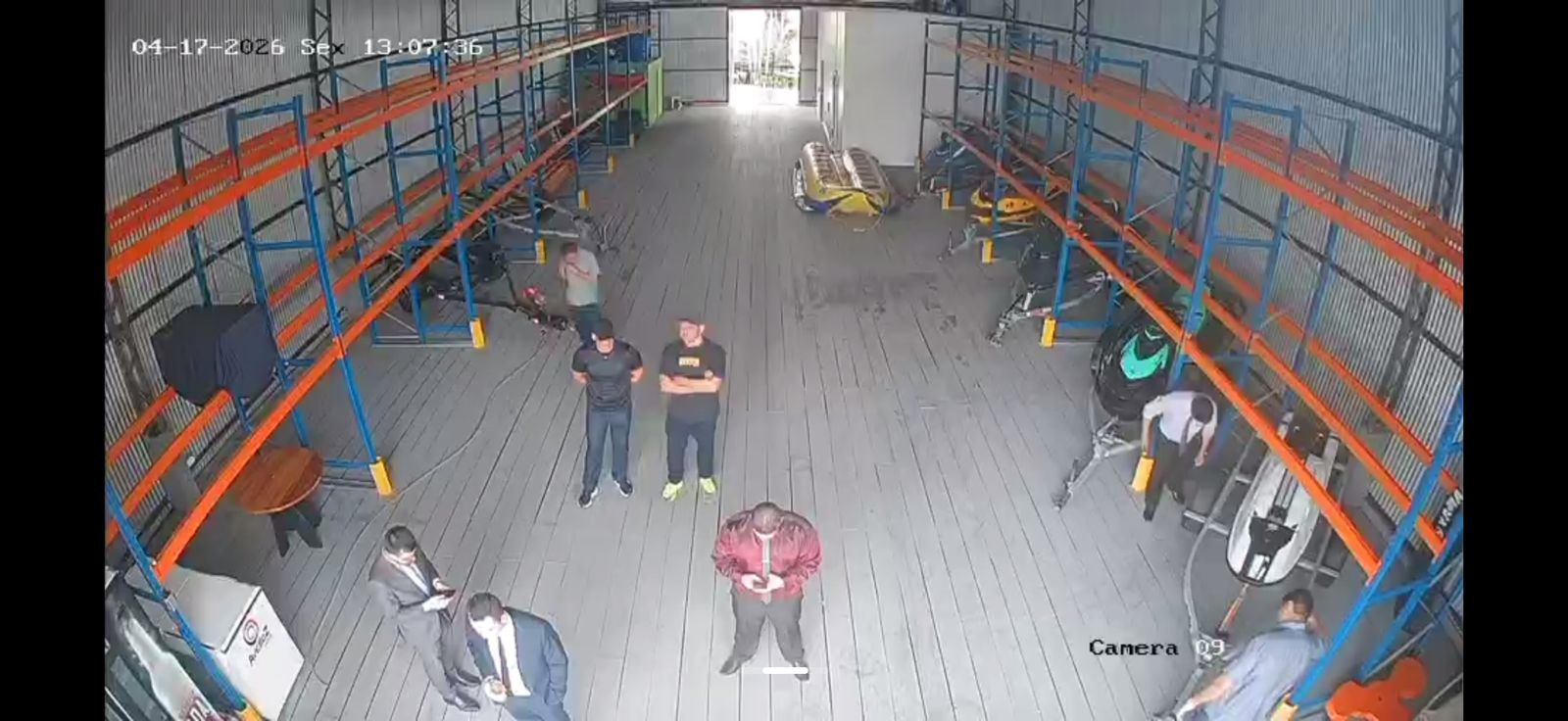 Câmera 09 da Marina Jet Marine. Grupo de homens trajados de social — entre eles os advogados reconhecidos pela vítima — concentrado no corredor central do galpão, ao lado das embarcações que seriam retiradas.